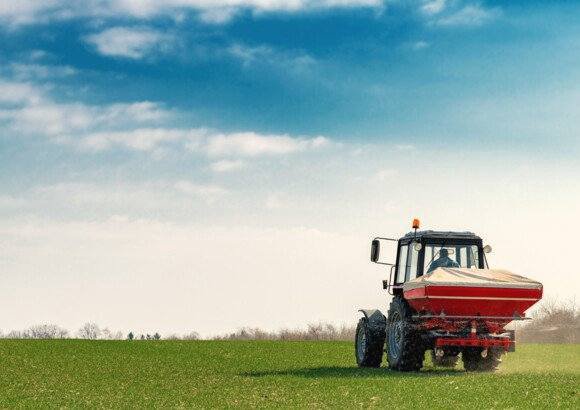 Trekker met kunstmeststrooier op grasland